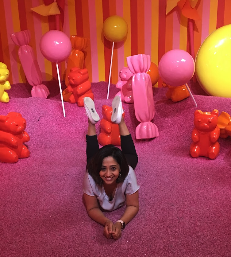 A woman smiling while lying on a pink floor in a colorful candy-themed room, representing the joy and freedom that can come from career transitions and successful job searching.